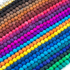 以下が含まれることがあります： 様々な色の溶岩ビーズのクローズアップ。ビーズは丸く、ざらざらとした多孔質の質感です。色は黒から緑、青、紫、赤、オレンジ、黄色まであります。
