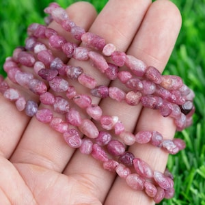 Op de afbeelding: Een streng roze en witte edelsteen kralen, met een gladde, afgeronde vorm. De kralen zijn geregen op een doorzichtige draad en zijn gerangschikt in een los, vloeiend patroon.