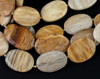 Puede incluir: Una hebra de cuentas de madera petrificada de forma ovalada en tonos marrones, beige y blancos. Las cuentas tienen un acabado natural y pulido y están enhebradas con un cordón fino de color crema.