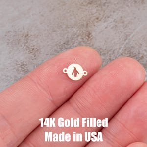 May include: A small, gold-colored charm with a penguin silhouette inside a circle. The charm has two small holes on either side. The text "14K Gold Filled Made in USA" is visible below the charm.