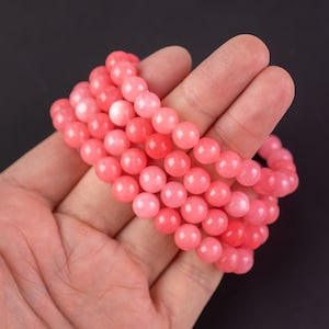 May include: A stack of pink and light pink beaded bracelets. The bracelets are made of round, smooth beads.