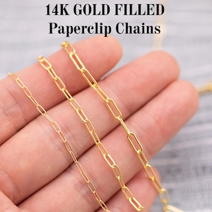 May include: Close-up of three gold-filled paperclip chains. The chains are displayed against a neutral background. The text "14K GOLD FILLED Paperclip Chains" is at the top of the image. The chains vary in size and link shape.
