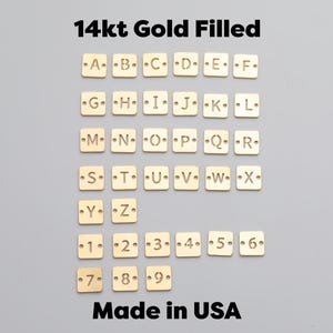 May include: Gold-filled square charms featuring letters A-Z and numbers 1-9, displayed on a grey background. The image also includes the text "14kt Gold Filled" and "Made in USA".