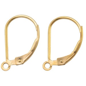 May include: Two gold-colored leverback earring findings. Each finding has a curved top, a straight post, and a hinged lever. The findings are designed for securing earrings.
