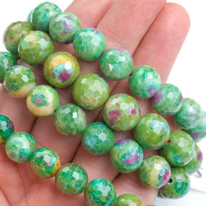 May include: A strand of green, faceted gemstone beads with pink and yellow inclusions. The beads are round and have a slightly irregular shape. The beads are strung on a clear thread.