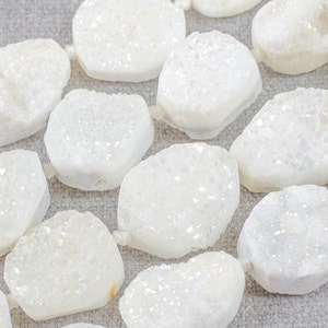 Op de afbeelding: Een streng witte, ondoorzichtige, ovale edelsteen kralen. De kralen hebben een ruw, getextureerd oppervlak en een licht iriserende glans.