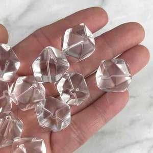 May include: A collection of clear, faceted, crystal beads in a variety of shapes. The beads are arranged in a hand, with some beads overlapping.
