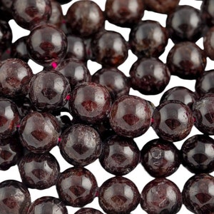 May include: A strand of dark red garnet beads. The beads are round and smooth, and they have a slightly shiny finish.