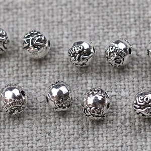 May include: Twelve silver beads with zodiac symbols, each bead is about 1 cm in diameter.
