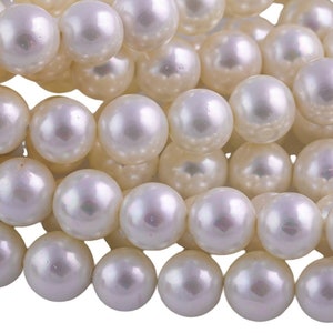 Op de afbeelding: Een streng witte parels, waarbij elke parel een gladde, glanzende afwerking heeft. De parels zijn in een los, overlappend patroon gerangschikt, wat een visueel aantrekkelijke textuur creëert.