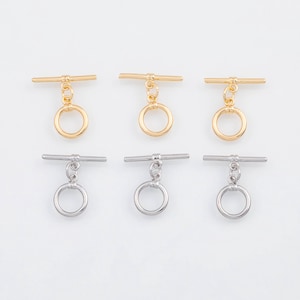 May include: Six toggle clasps are shown, three gold and three silver, on a white backdrop. Each clasp features a horizontal bar and a circular ring, suitable for jewellery making and various craft projects.