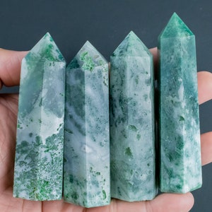 Puede incluir: Cinco puntas de cristal de ágata verde y blanco, también conocidas como varitas, se sostienen en una mano. Las puntas son lisas y pulidas, con una variedad de patrones verdes y blancos.