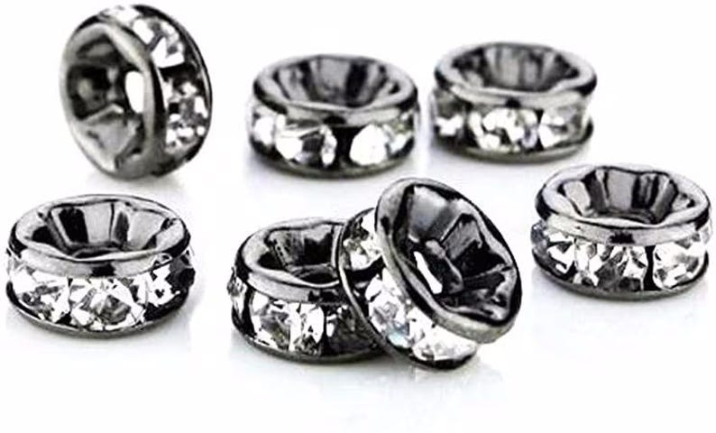 May include: A collection of six round, gunmetal-toned metal spacer beads. Each bead features a central hole and is embedded with a row of clear, faceted crystals around the outer circumference, creating a reflective and textured appearance.