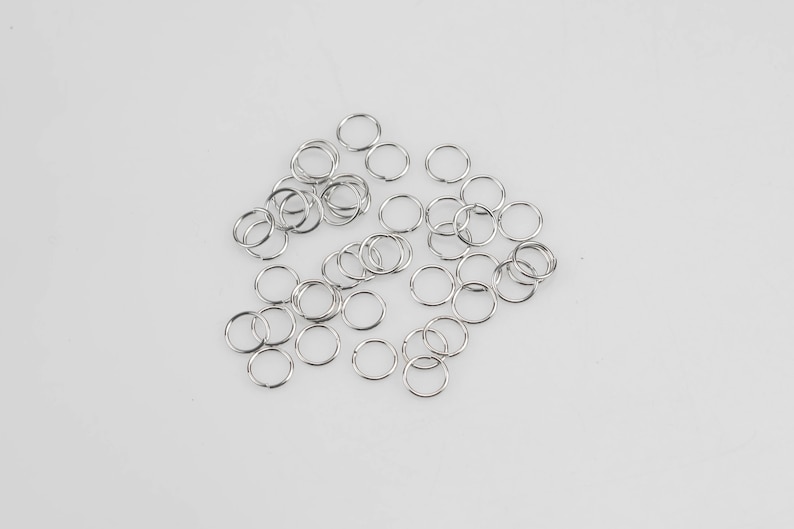 May include: A pile of silver jump rings, a type of metal ring used for jewelry making.
