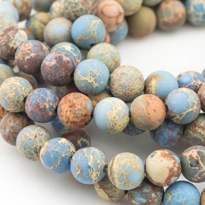 May include: A strand of blue, brown, and beige jasper beads. The beads are round and have a mottled pattern.
