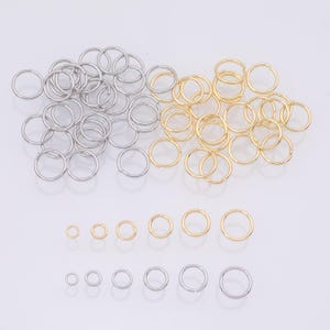 May include: An assortment of silver and gold-colored metal rings of varying sizes. The rings are arranged in groups, with smaller rings lined up at the bottom. The jewelry pieces are likely for piercings or crafting.