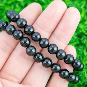 May include: A black beaded bracelet with two rows of round beads. The bracelet is shown on a hand against a green background.
