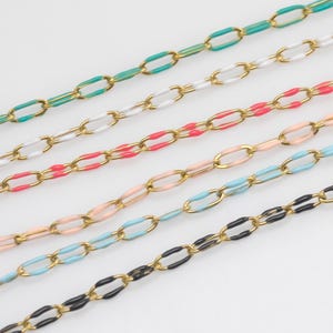 May include: Close-up of several colourful chain necklaces. Each chain features gold-coloured links with enamel in various colours, including teal, white, red, peach, light blue, and black. The chains are arranged diagonally against a white background.