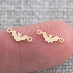 以下が含まれることがあります： ジャンプリングが付いた金色の金属製のバットチャーム2個。チャームは、翼を広げたバットの形をしています。
