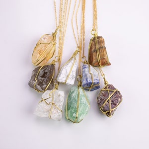 May include: A selection of gemstone necklaces. Each necklace features a raw gemstone pendant, wrapped in gold-coloured wire and suspended from a gold chain. The gemstones are various colours, including clear, green, purple, brown, and white.