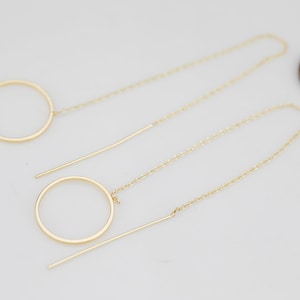May include: A pair of gold earrings with a circle design. Each earring has a small circle and a larger circle connected by a thin chain.