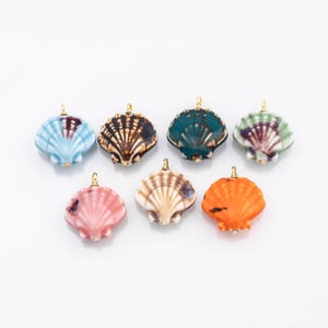 May include: A collection of seven seashell pendants in various colors, including blue, brown, teal, green, pink, tan, and orange. Each pendant has a gold-colored bail for attaching to a chain or cord. The pendants are arranged on a white background.