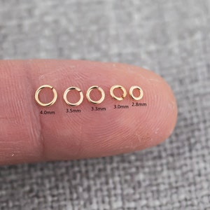 May include: A close-up of six gold jump rings of different sizes, ranging from 2.8 mm to 4.0 mm in diameter. The rings are arranged in a row on a finger.