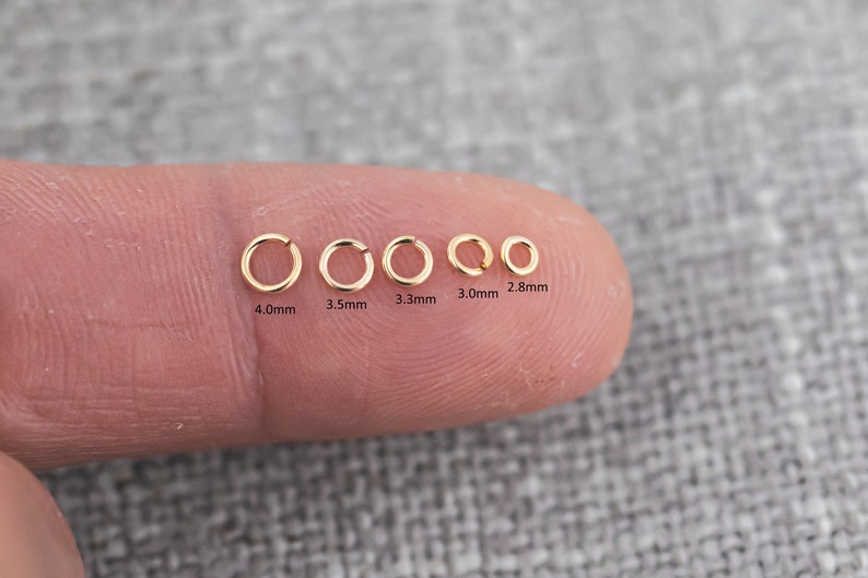 May include: A close-up of six gold jump rings of different sizes, ranging from 2.8 mm to 4.0 mm in diameter. The rings are arranged in a row on a finger.