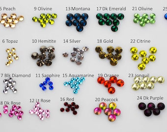 May include: Assortment of 28 different colors of rhinestones, labeled with numbers and names.  The colors include clear, black, silver, gold, red, blue, green, purple, orange, yellow, and brown.