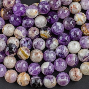 May include: A strand of round, purple amethyst beads with white and brown inclusions. The beads are polished and have a smooth, glossy finish.