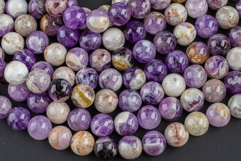 May include: A strand of round, purple amethyst beads with white and brown inclusions. The beads are polished and have a smooth, glossy finish.