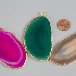 May include: Three agate slices with gold trim, each with a different color pattern: pink, green, and brown. The slices are about the size of a US quarter.