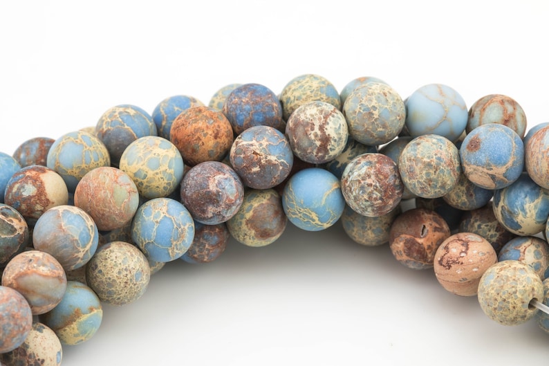 May include: A strand of blue, brown, and beige jasper beads. The beads are round and have a mottled pattern.