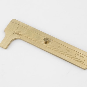 May include: A brass caliper with a measurement scale up to 70 mm.
