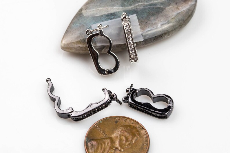 May include: Two silver and black metal clasps with clear crystal accents. The clasps are designed to be used as jewelry closures.