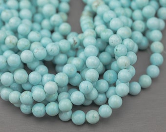 May include: Close-up of strands of light blue round beads. The beads have a matte finish and are strung together, creating a flowing, organic shape. The beads are a consistent size and color, with subtle variations.