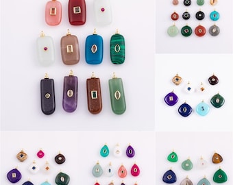 May include: A collection of gemstone pendants in various shapes and colors, including rectangular, oval, and teardrop designs. Each pendant features a gold-colored bail for hanging and is set against a white background.