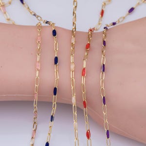 May include: A gold-toned chain necklace featuring elongated oval links interspersed with small, smooth, cylindrical enamel accents in various colors including light pink, dark blue, cream, bright red, and deep purple.
