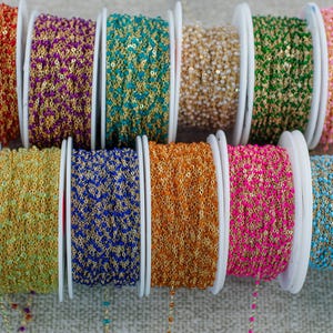 May include: A selection of colourful beaded chain spools. The spools display a variety of colours, including red, purple, teal, gold, green, pink, fuchsia, yellow, blue, orange, and turquoise. Each spool is filled with a beaded chain, ideal for jewellery making and crafting.