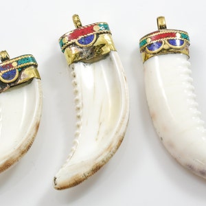 May include: Three white tooth-shaped pendants with gold, red, blue, and green enamel accents. The pendants are different sizes and have a decorative design.