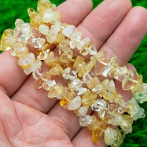 May include: A strand of yellow and clear chip gemstone beads. The beads are irregular in shape and have a natural, rough texture.