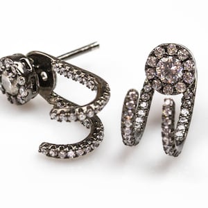 May include: A pair of black ear cuffs with a single round clear stone surrounded by smaller stones. The ear cuffs are made of metal and have a curved design.