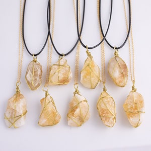 May include: A selection of citrine crystal necklaces. Each necklace has a raw, golden-yellow citrine stone wrapped in gold-coloured wire, suspended from a gold chain and a black cord. The crystals vary in size and shape.