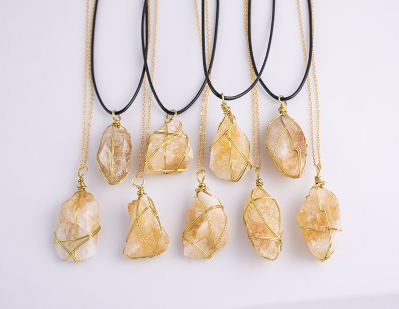May include: A selection of citrine crystal necklaces. Each necklace has a raw, golden-yellow citrine stone wrapped in gold-coloured wire, suspended from a gold chain and a black cord. The crystals vary in size and shape.