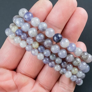 May include: A stack of four bracelets made with round, light blue, lavender, and gray gemstone beads.