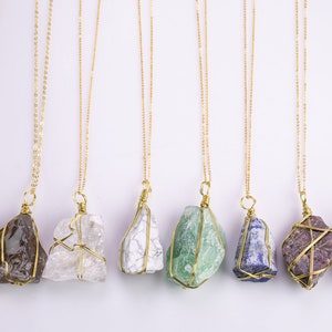 May include: A selection of gold chain necklaces, each with a distinctive, irregularly shaped gemstone pendant. The pendants display a variety of colours, including brown, clear, white, green, blue, purple, and tan. The gemstones are held in place by a gold wire cage.