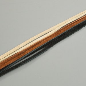 May include: A close-up of a leather cord with three strands in black, brown, and cream colors.