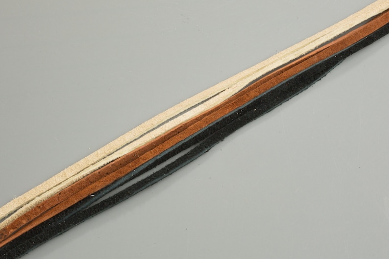 May include: A close-up of a leather cord with three strands in black, brown, and cream colors.