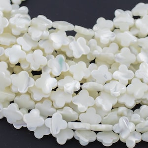 May include: Close-up of a collection of white, four-petal flower-shaped beads. The beads have a pearlescent sheen and are strung together. These beads are ideal for jewelry making and crafting projects.