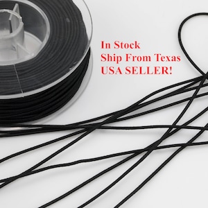 May include: A spool of black elastic cord, wound around a clear plastic spool. The cord is lying on a white surface.